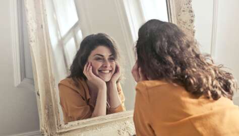 Junge Frau betrachtet sich fröhlich in einem stylischen alten Spiegel